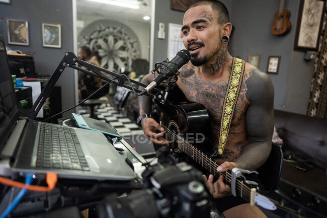 Asian guy playing guitar in studio and singing — Stock Photo