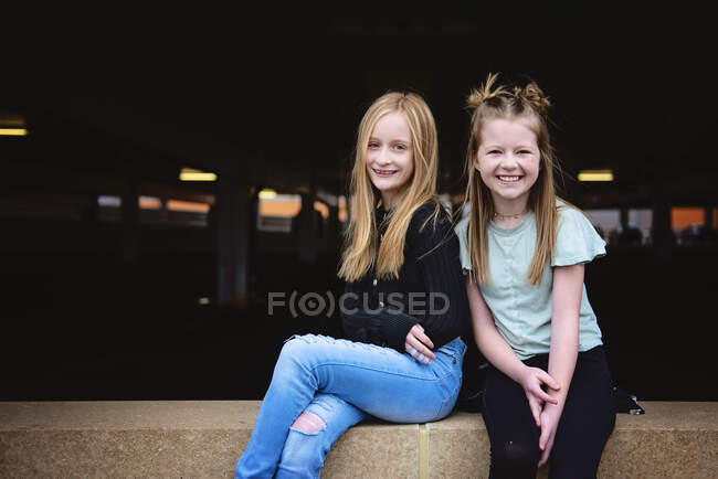 Zwei glückliche Zwillingsmädchen sitzen zusammen auf einer Ziegelwand. — Stockfoto