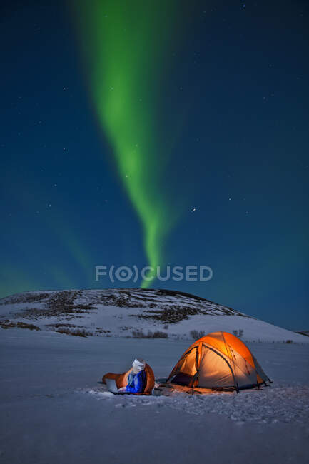 Wissenschaftlerin sitzt vor ihrem Zelt mit Nordlichtern am Himmel — Stockfoto