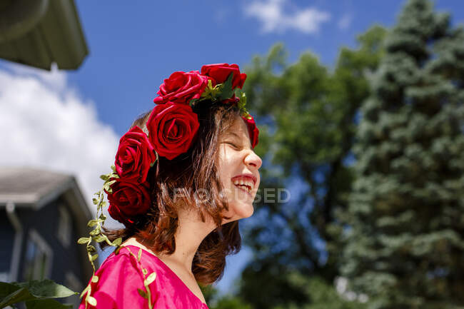 A laughing little girl with closed eyes wears a crown of roses — Stock Photo