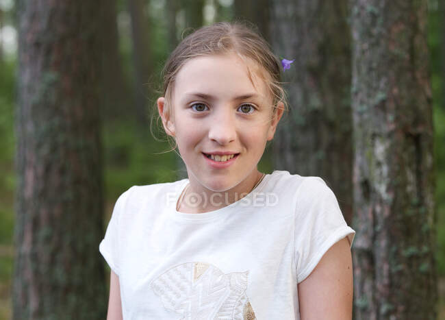 Retrato de niña sonriente con flor en el pelo en el bosque - foto de stock