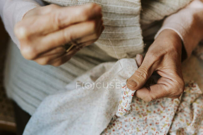 Primer plano de las manos de la mujer cosiendo con aguja e hilo - foto de stock