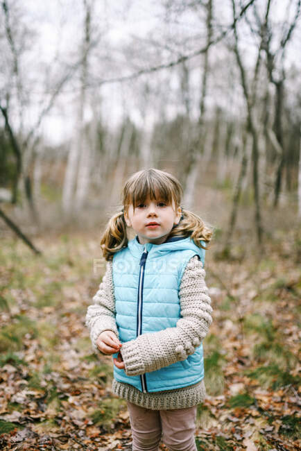 Little girl standing in the woods in spring wearing a light teal vest — Stock Photo