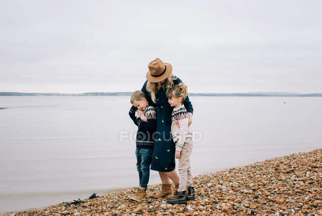 Mutter und ihre Kinder gehen am Strand entlang und umarmen sich an einem ruhigen Herbsttag — Stockfoto