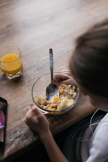 Das Mädchen frühstückt und schaut auf das Telefon — Stockfoto