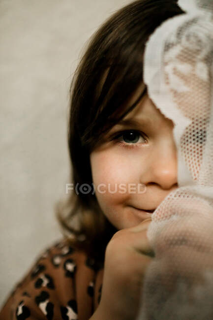 Young girl holding up lace curtain covering half of her face — Stock Photo