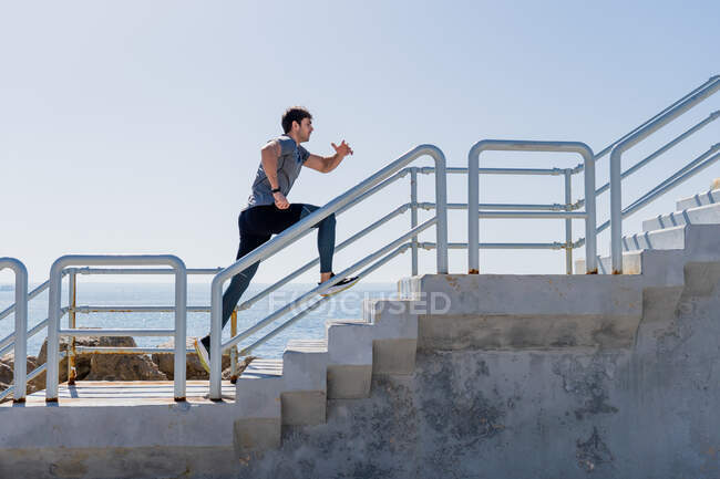 Profile of young man running upstairs outside with clear sky at port — Stock Photo