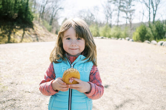 Маленькая девочка с широкой улыбкой на лице позирует с пончиком в руке — стоковое фото