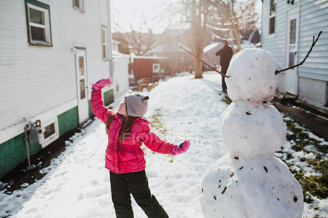 Young girl poses with her snowman after a spring snowfall — Stock Photo