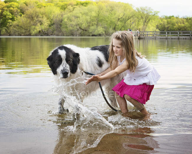 Jovem brincando em um lago com um cachorro da Terra Nova — Fotografia de Stock