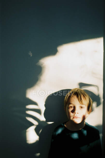 Маленький мальчик с тенями на лице и за стеной — стоковое фото