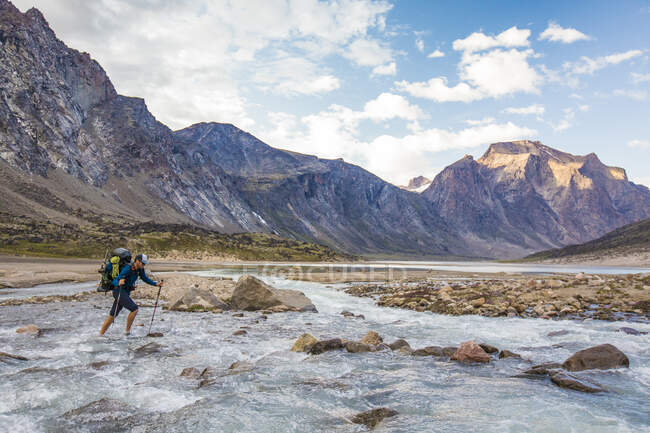 Montañero cruza un río furioso en un paso de montaña - foto de stock