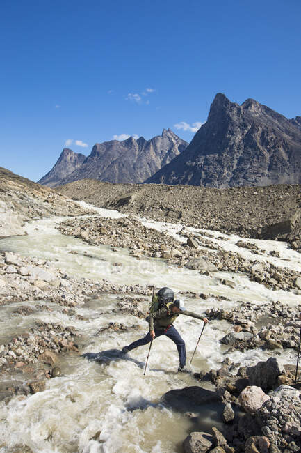 Backpacker steps across a raging river, Akshayak Pass. — Stock Photo