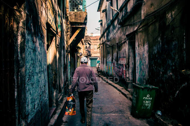 Человек с пакетом ходить по узкой улице — стоковое фото