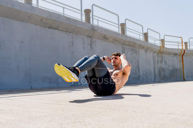 Young man doing sit-ups without a shirt on the street at noon — Stock Photo