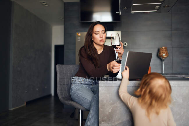 Mujer morena bebiendo vino y utilizando el ordenador portátil - foto de stock