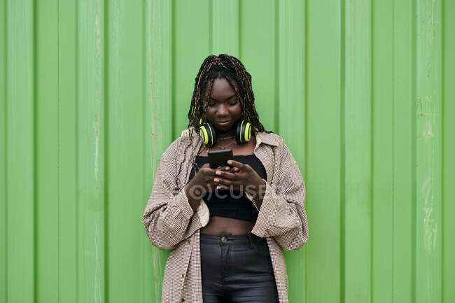 Mulher negra em roupas urbanas olhando para o seu celular enquanto ela sorri — Fotografia de Stock