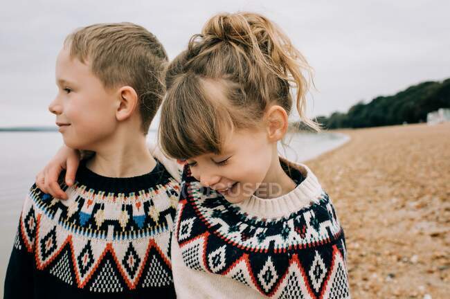 Hermanos abrazándose y riendo juntos en la playa en el Reino Unido - foto de stock