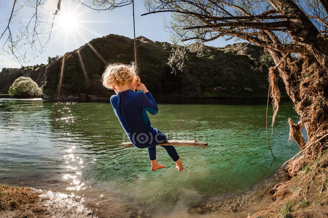 Blondes Kind an sonnigem Tag auf Schaukel über Fluss in Neuseeland — Stockfoto