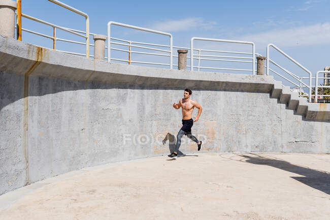 Jeune homme courant torse nu autour d'un mur à l'extérieur avec un ciel clair — Photo de stock