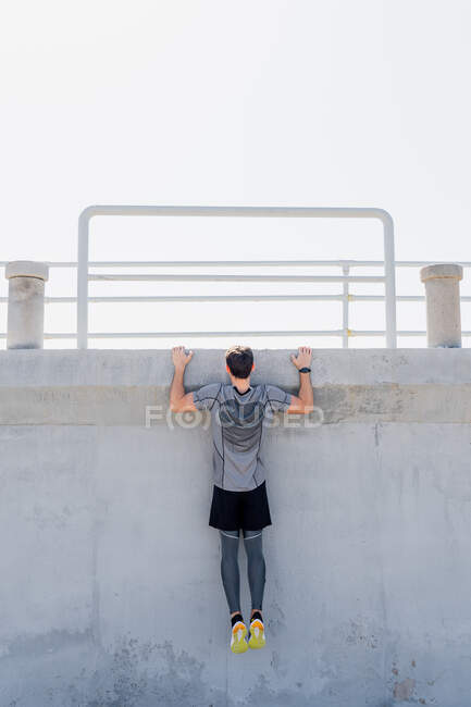 Man doing pull-ups outdoors grabs a wall with clear sky at noon — Stock Photo