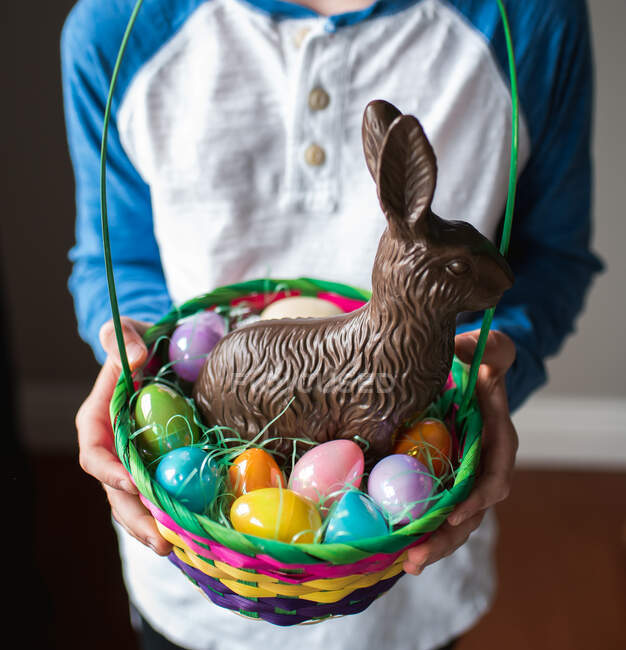 Gros plan des mains de l'enfant tenant un panier de Pâques rempli de friandises. — Photo de stock
