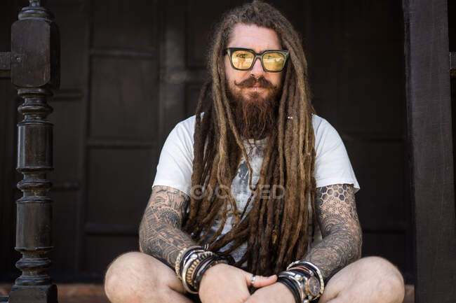 Hipster guy avec dreadlocks et tatouage assis sur la plage en thailan — Photo de stock
