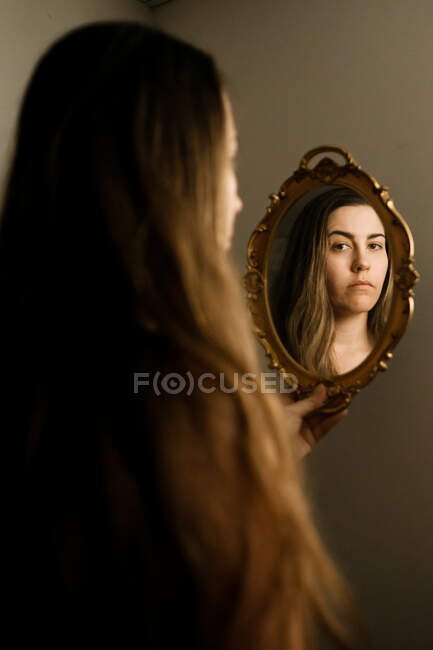 Женщина, смотрящая на себя в винтажное зеркало — стоковое фото
