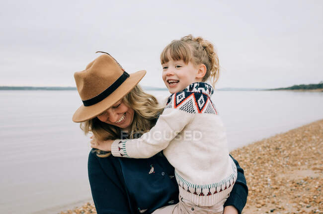 Mamma e figlia ridono insieme mentre camminano sulla spiaggia in autunno — Foto stock