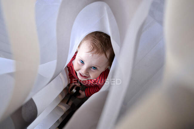 Улыбающаяся маленькая девочка прячется в занавесках — стоковое фото