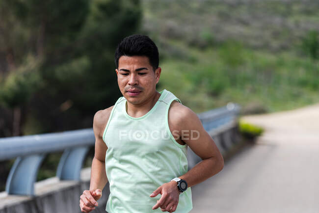 Primer plano de un joven corredor latinoamericano corriendo sobre un puente. - foto de stock