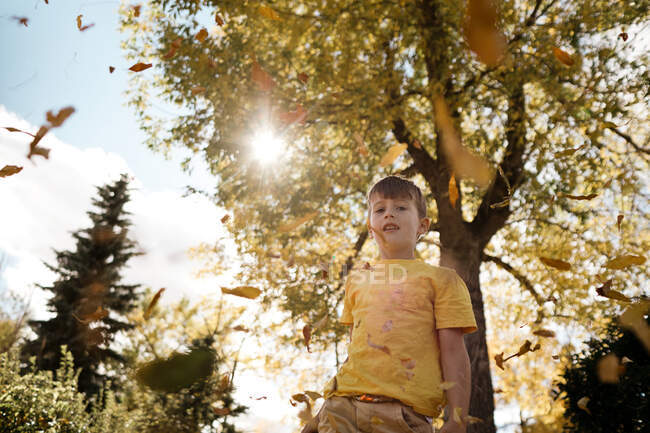Jeune garçon habillé en jaune jouant dans les feuilles à l'automne — Photo de stock