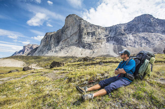 Backpacker resting, sitting in grassy meadow below mountain summit. — Stock Photo