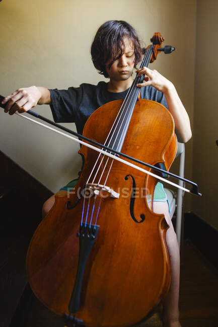 Крупный план мальчика с интенсивным фокусом, играющего на виолончели на лестнице — стоковое фото