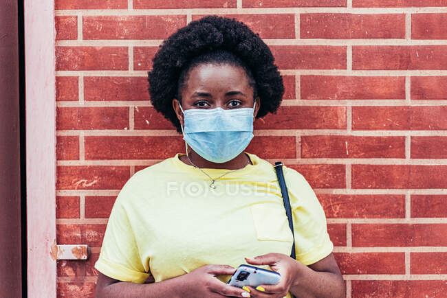 Портрет афроамериканской девушки в маске на фоне стены из красного кирпича. — стоковое фото