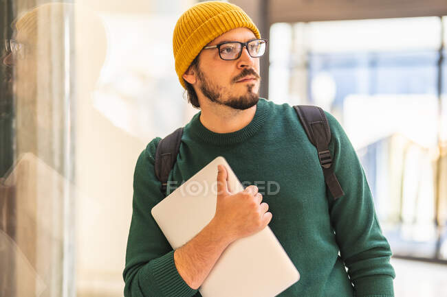 Hombre español moderno con gafas y portátil posando en un centro comercial - foto de stock