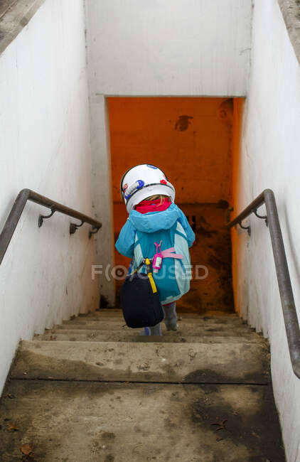 Маленький ребенок в космическом шлеме и рюкзаке спускается по лестнице в туннель — стоковое фото