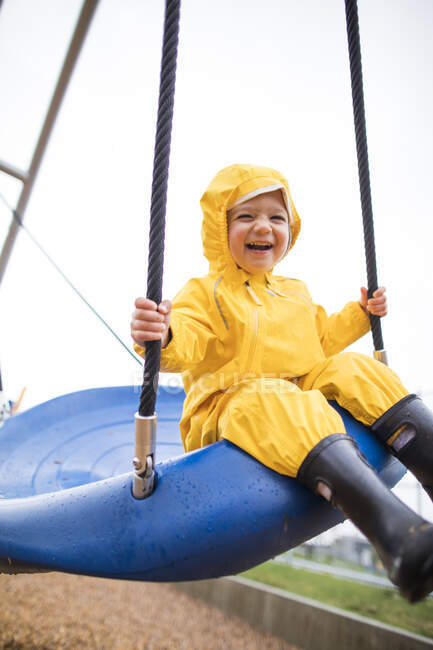 Joyeux tout-petit garçon monte sur balançoire au parc par une journée humide — Photo de stock