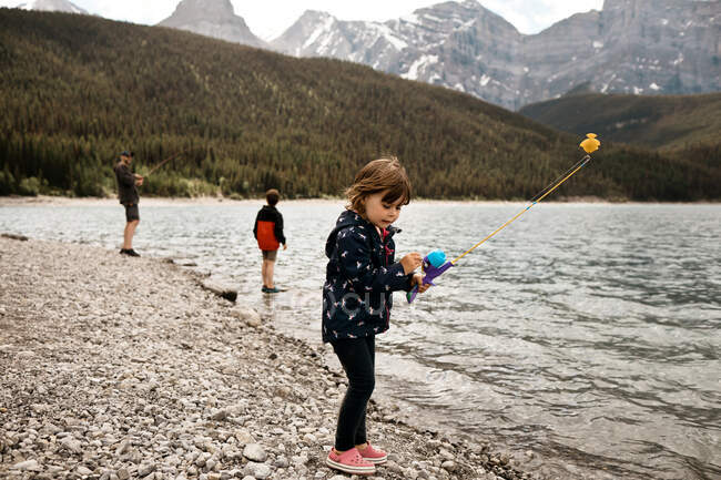 Jovem pesca menina com seu pai e irmão em um lago de montanha — Fotografia de Stock