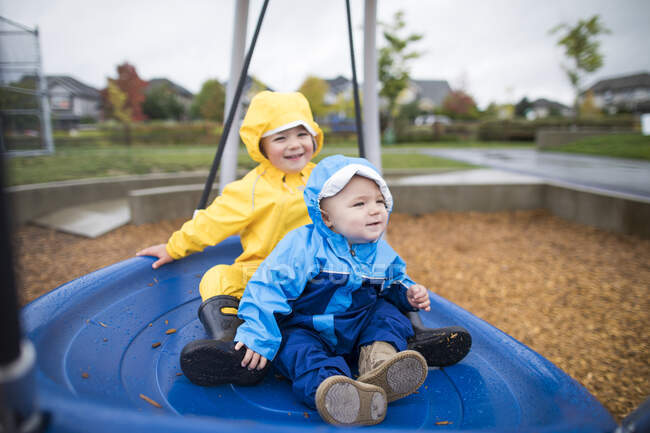 Двое детей сидят на больших голубых качелях в парке — стоковое фото