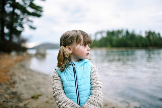 Petite fille tout-petit avec des tresses sur le rivage regardant vers le lac — Photo de stock