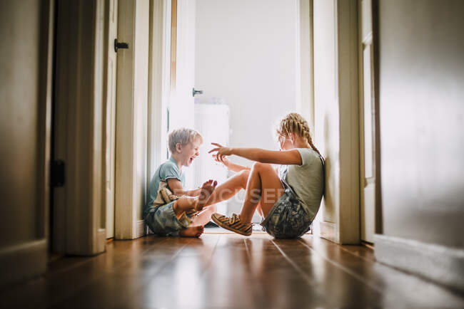 Брат и сестра играют и смеются в светлом коридоре — стоковое фото