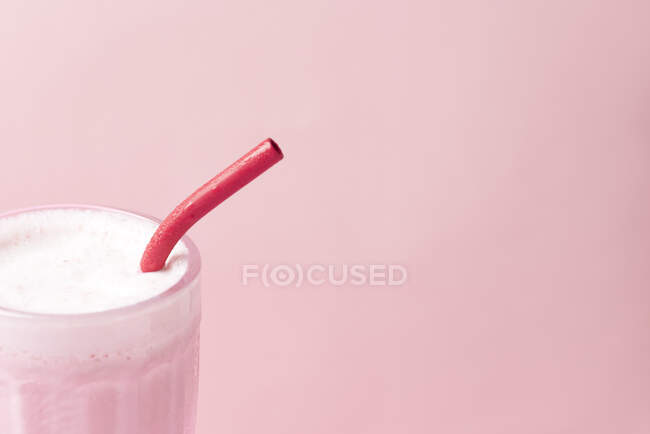 Close up view of a raspberry milkshake served in a dessert glass with a reusable eco-friendly metal straw. Pastel pink color background with copy space. — Stock Photo