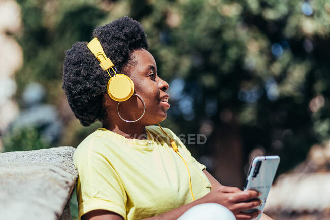 Chica afroamericana escuchando música con su teléfono celular y auriculares. - foto de stock