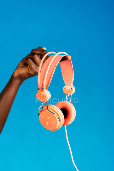 Main de femme anonyme tenant des écouteurs orange sur fond bleu — Photo de stock