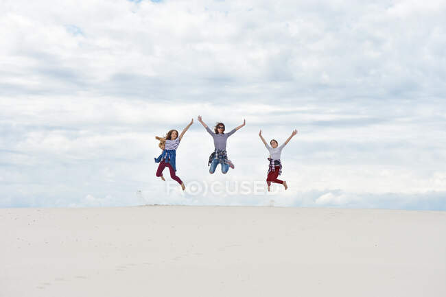 Las niñas con mamá están saltando sobre el fondo del cielo y la arena - foto de stock