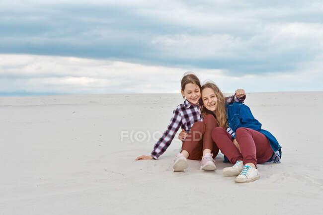 The sisters are hugging while sitting on the sandy slope. — Stock Photo