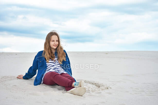Adolescente sentada en la arena y mirando a la distancia - foto de stock