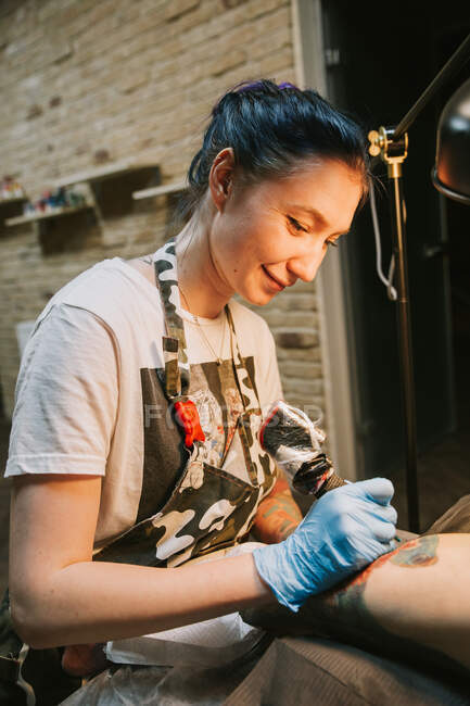 Portrait of a woman tattoo master showing a process of creation tattoo on a hand under the lamp light — Stock Photo