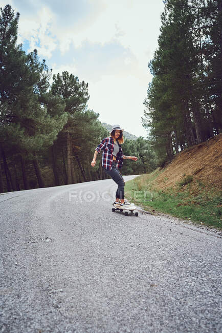 Una mujer con un monopatín en un camino de montaña - foto de stock